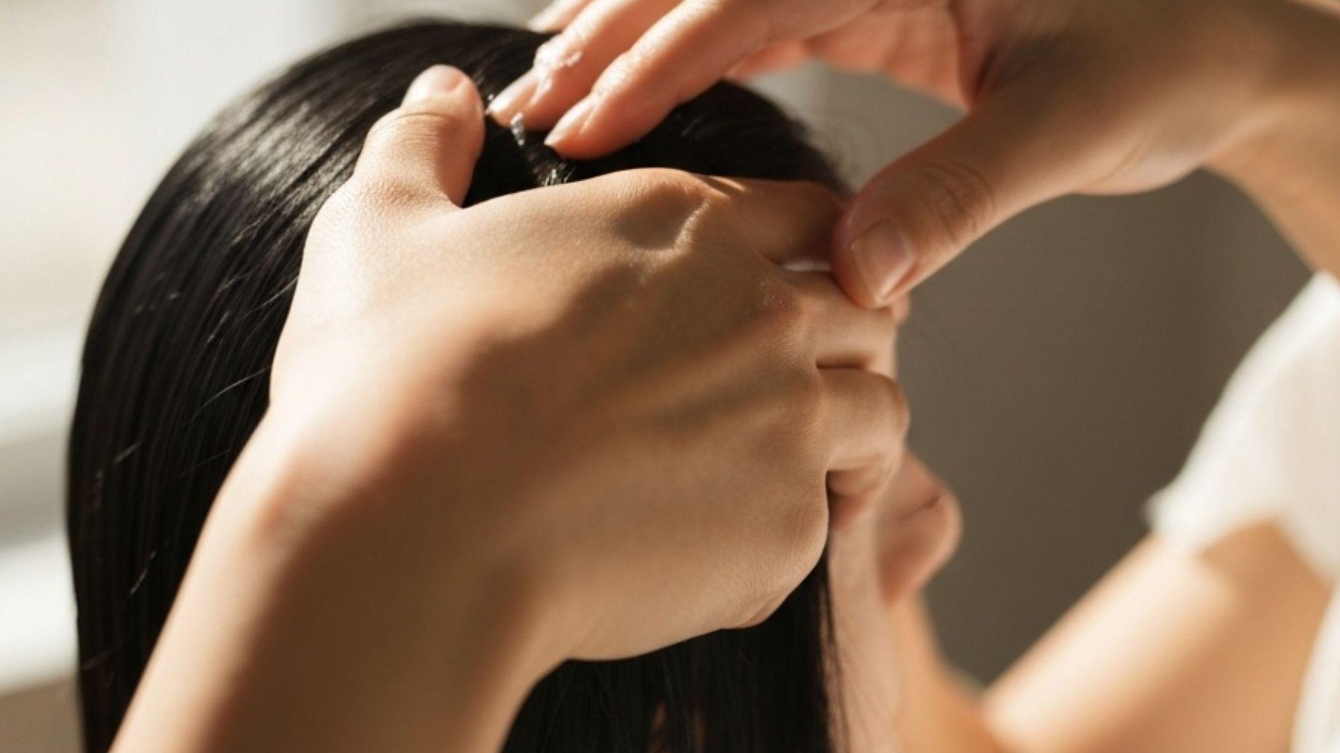 Nærbilde av hender som masserer hodebunn-behandling inn i rent hår i varmt naturlig vinduslys, editorial wellness-stil